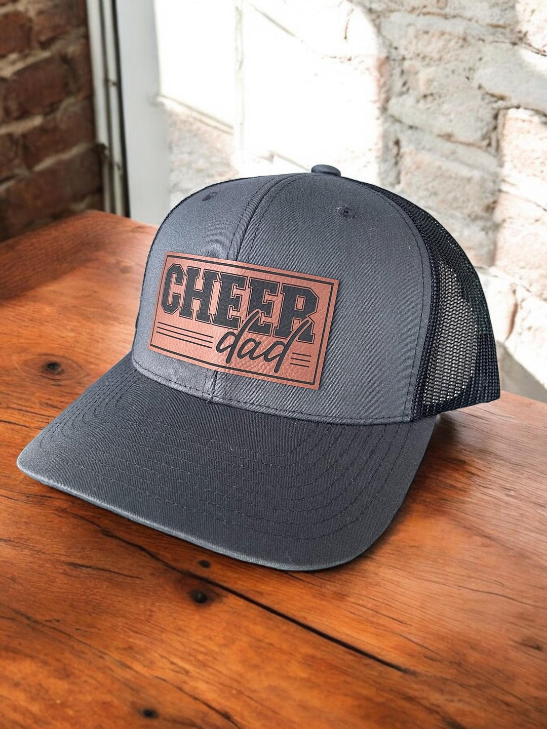 Cheer Dad Trucker Hat featuring an adjustable snapback and breathable black mesh back. Available with a bold &#39;Cheer Dad&#39; patch. Perfect for proud dads supporting their cheerleaders on game day.
